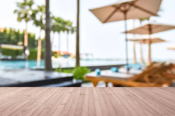 Wood floor with blur summer background tropical resort hotel with blue swimming pool and palm tree