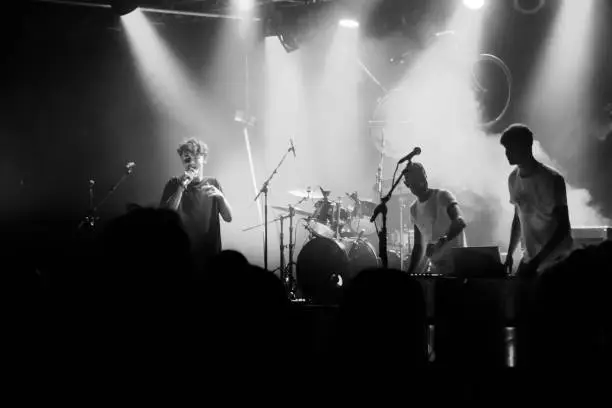 Young music rock band on the stage. Teenage group are making music, and are in love with it. Shoot with artificial light and stage light inside. The group of young people, are shoot in Denmark in black and white, B&W. The teenagers are singing, jumping and playing on their instruments.