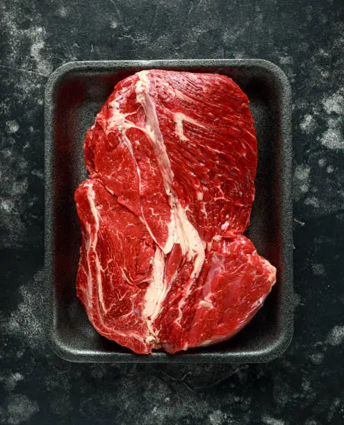 Fresh Raw braising steak on black tray.