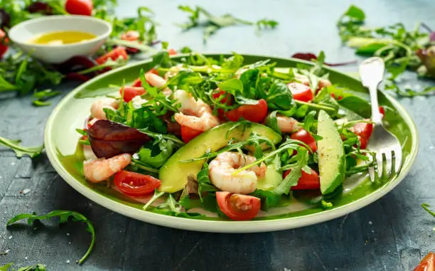 Fresh Avocado, shrimps salad with lettuce green mix, cherry tomatoes, herbs and olive oil, lemon dressing. healthy food.