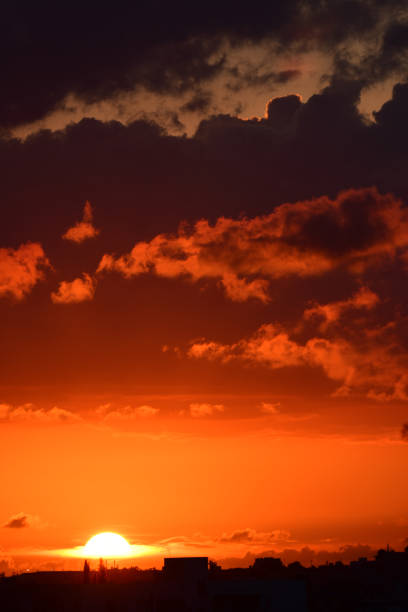 istock Orange sunset with sun plunging through clouds on horizon 990316764