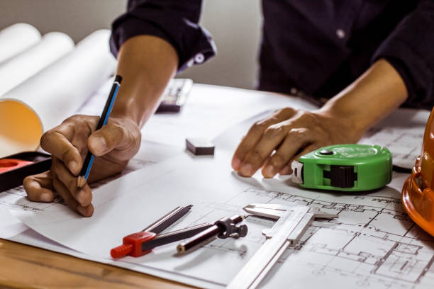 istock Concept architects,engineer holding pen pointing equipment architects On the desk with a blueprint in the office, Vintage, Sunset light.Selective Focus 990319718