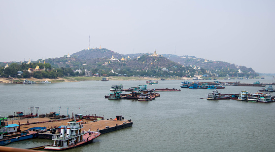 Golden pagodas and monasteries dot the landscape of Sagaing Hill, with the Irrawaddy River filled with barges and boats in the foreground.