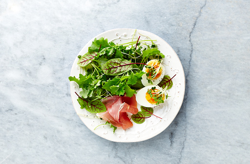 Mixed leaf salad with egg, serrano ham, and herbs. Healthy diet. Flat lay. Home made food