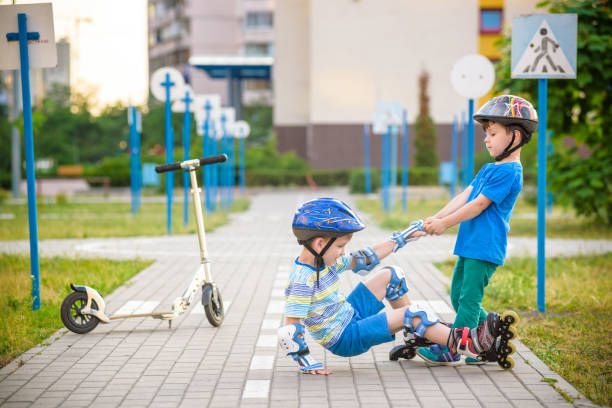 istock two boys in park, help boy with roller skates to stand up 990361064