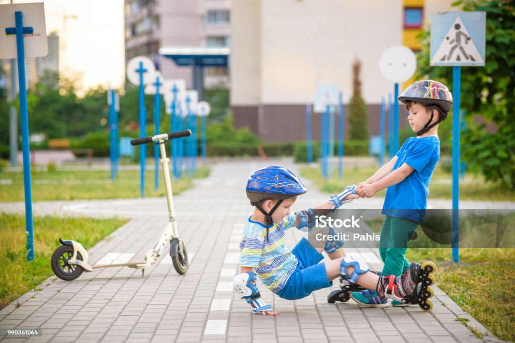 two boys in park, help boy with roller skates to stand up Two boys sibling brothers together in park, helps boy with roller skates to stand up after fall. Friendship and active leisure summer holidays time with family concept. Assistance Stock Photo