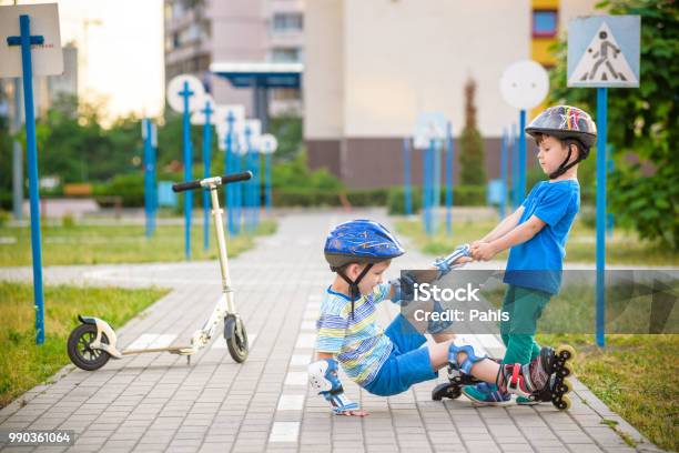 Two Boys In Park Help Boy With Roller Skates To Stand Up Stock Photo - Download Image Now