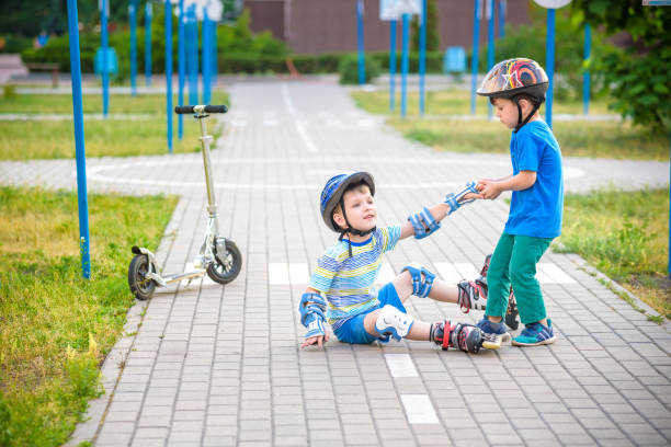istock two boys in park, help boy with roller skates to stand up 990361126