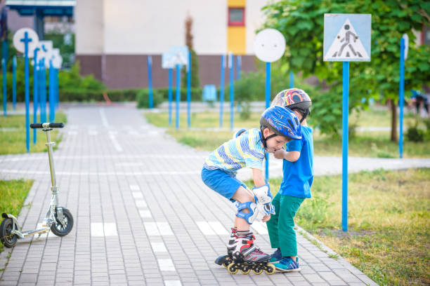 istock two boys in park, help boy with roller skates to stand up 990361202