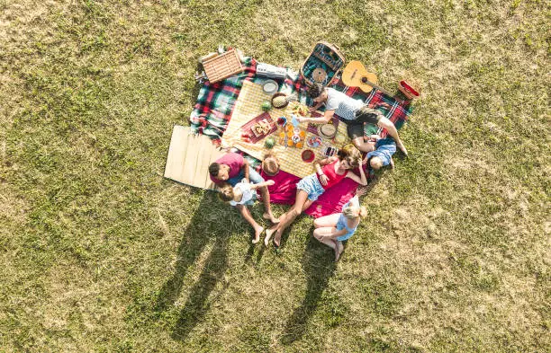 Aerial drone view of happy families having fun with kids at picnic barbecue party - Multiracial happiness and love concept with mixed race people playing with children at park - Warm bright filter