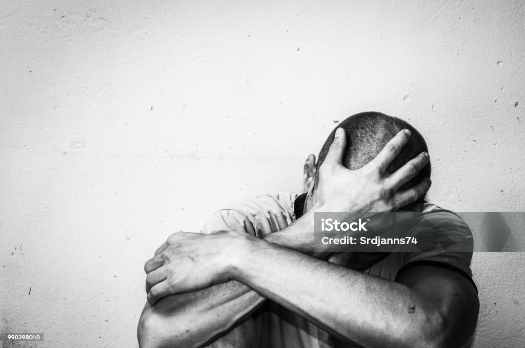 Homeless man drug and alcohol addict sitting alone and depressed on the street feeling anxious and lonely, social documentary concept black and white Depression - Sadness Stock Photo