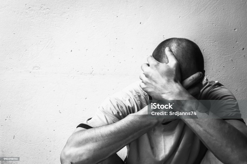 Homeless man drug and alcohol addict sitting alone and depressed on the street feeling anxious and lonely, social documentary concept black and white Addiction Stock Photo