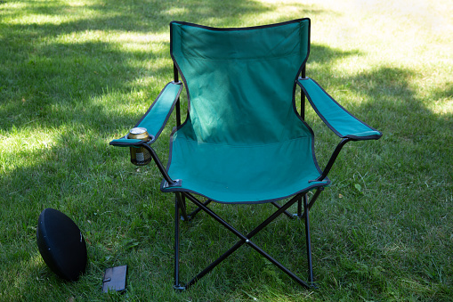 Folding chair standing on grass field with drinking can, wireless loudspeaker and smartphone for relax time in summer.