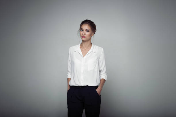Interested businesswoman with trendy makeup posing on gray background in studio. Indoor photo of serious young lady in white blouses classic black pants standing in confident pose. Interested businesswoman with trendy makeup posing on gray background in studio. Indoor photo of serious young lady in white blouses classic black pants standing in confident pose blouse stock pictures, royalty-free photos & images