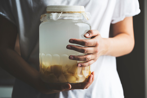 Woman holding apple cider vinegar in jar covered with cheesecloth