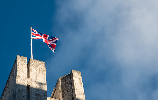 British flag waving against a blue cloudy sky on the top of a building in London UK