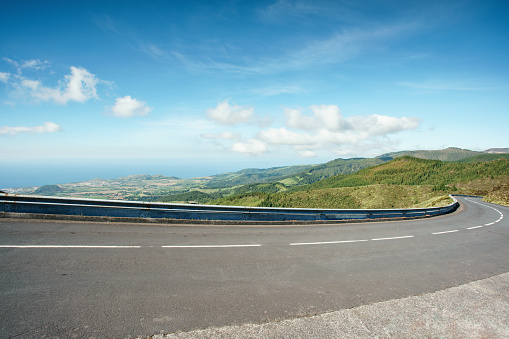 Turning mountain highway with blue sky and sea on a background. A curvy road through the grassy hills with a view of the ocean.