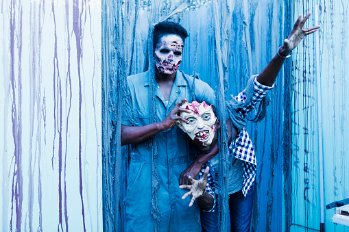 Two young African-American men dressed up as zombies and monsters, scaring people in a halloween haunted house.