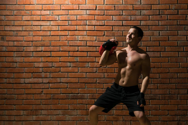 an athlete shows how to do an exercise with the weight to form a muscle in the fitness room on a red wall background - healthy lifestyle men boxing dumbbell imagens e fotografias de stock