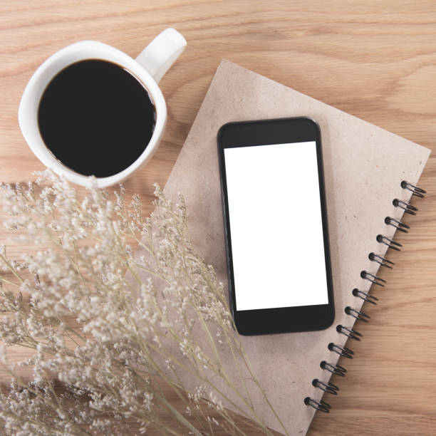 istock Mobile phone with blank screen with book, green leaf, and coffee cup on wooden table background. 990479190