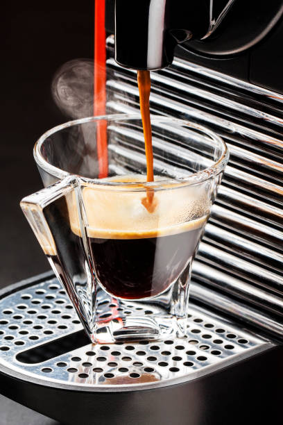 istock Closeup coffee maker pouring hot coffee espresso into glass cup 990479988