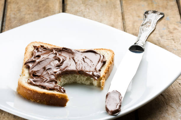 istock slice of toast with hazelnut chocolate spread, a bite taken, on a white plate next to silver knife on rustic wooden table 990480032