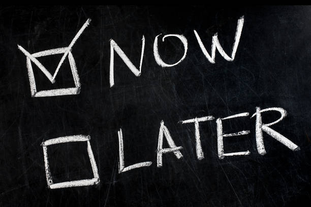 istock Now and Later check boxes handwritten with white chalk on blackboard 990480042
