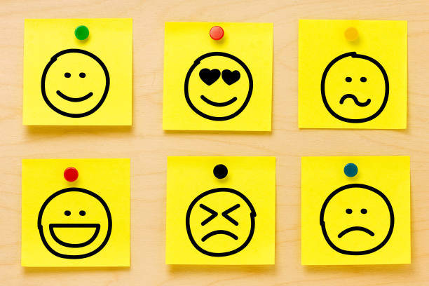 istock Hand drawing emoticons on six yellow postit notes affixed by colored pins on a wooden board 990480458