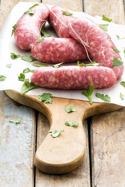 istock Raw sausages with herbs on baking sheet on catting board on rustic wooden table 990491796