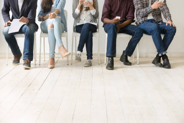 Bottom view of diverse work candidates waiting for job interview Close up view of diverse work applicants sitting together, holding smartphones, tablets and papers getting ready for interview, multiethnic candidates waiting in queue. Employment, hiring concept unemployment stock pictures, royalty-free photos & images