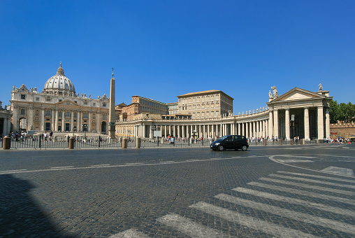 St. Peter's Basilica is an Italian Renaissance church in Vatican City and the papal residence within the city of Rome, Italy. St. Sightseeing tourists, street lamps and blue sky with are in the image. Wide angle lens.