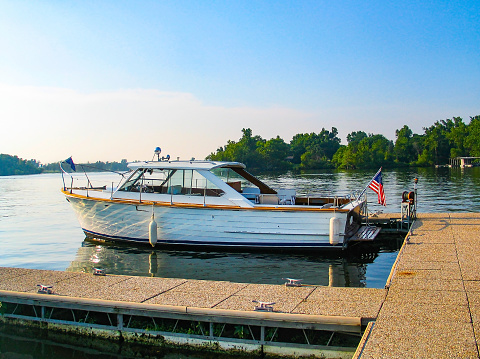 This August 2022 panoramic image shows the sunrise at Lake of Two Rivers in Algonquin Provincial Park, Ontario, Canada. A red canoe with wooden oars sits on a dock in the foreground. In the background, the morning sun rises over a forested hill. Mist hugs the surface of the lake, as low clouds reflect multiple colors in the dawn sky.