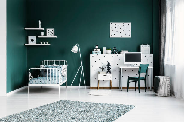 istock Spacious bedroom interior with a single bed, lamp, shelves, desk with a computer and rug 990538318
