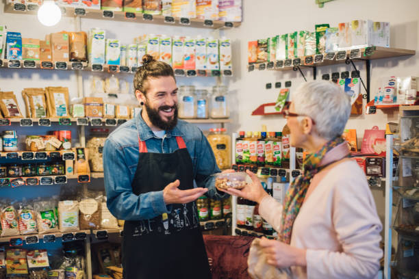 Happy sales man handing a pack of nuts to a customer Senior woman buying at the healthy food store retail place stock pictures, royalty-free photos & images