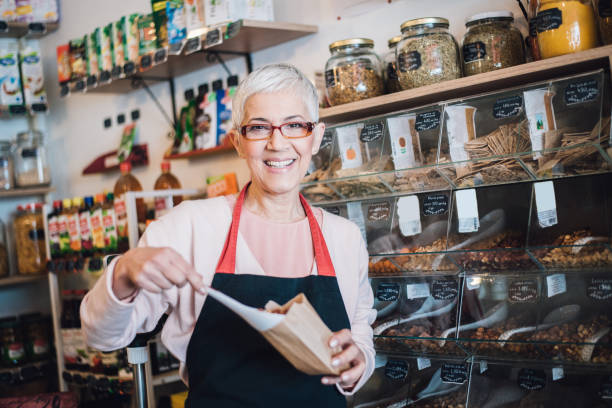 happy sales woman pouring nuts in paper bag - organic spice imagens e fotografias de stock