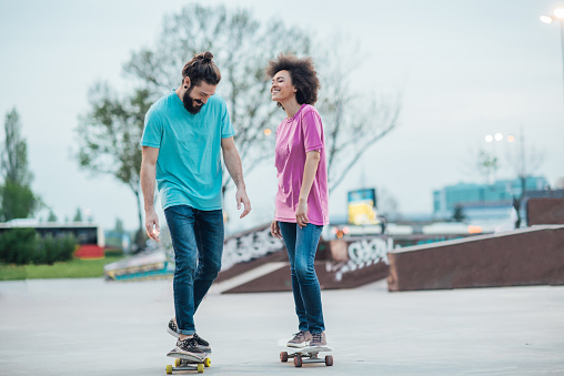 Happy couple riding skateboards at skate park