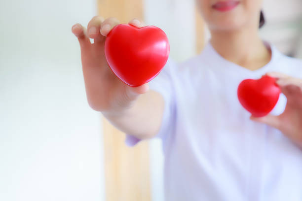 istock Red heart held by smiling female nurse's hand, representing giving effort high quality service mind to patient. Professional, Specialist in white uniform concept 990562072