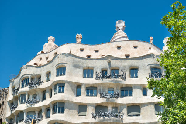 BARCELONA, SPAIN - May 21, 2016: Facade of Casa Mila with green trees on the street of Barcelona, Spain. Famous building designed by Antoni Gaudi, included in the UNESCO list