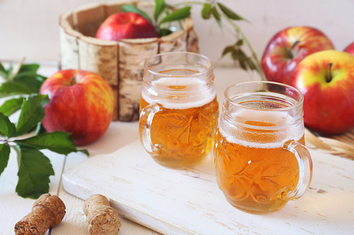 Two cups of Apple Cider and red apples in wooden  basket on light background