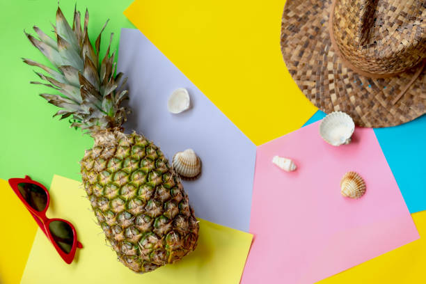 istock Whole pineapple on colorful background with hat, glasses, seashells, top view. Modern summer concept 990630262