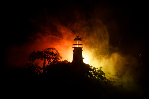 Lighthouse with light beam at night with fog. Old lighthouse standing on mountain. Table decoration. Toned background. Moonlighting. Selective focus