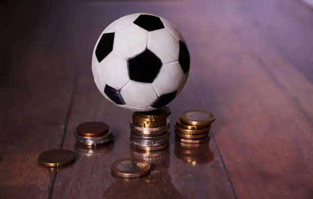 A Football or soccer ball and a pile of money on a Wooden background