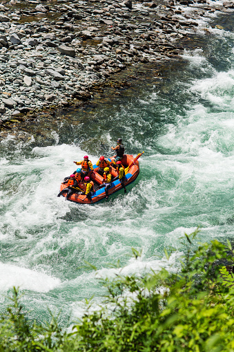 Group of men and women white water river rafting in a forested valley in Japan.