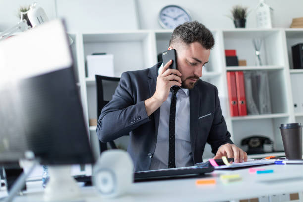 istock A man is sitting in the office at the desk, talking on the phone and working with documents and a calculator. 990659178