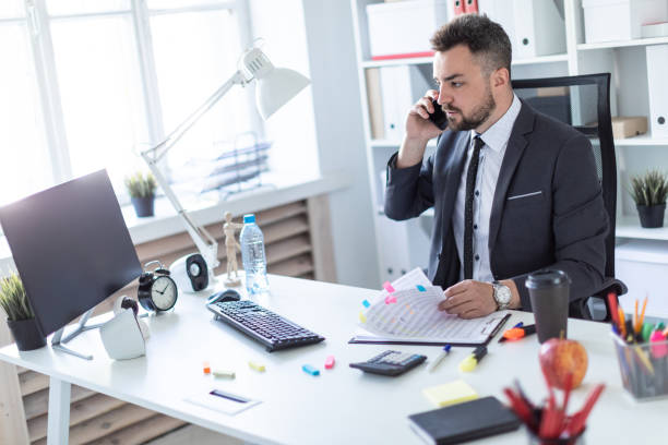 istock A man is sitting in the office at the table, talking on the phone and flipping through documents. 990659190
