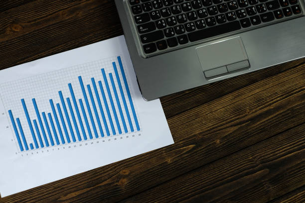 istock Notebook laptop computer and financial graph on white paper on working table, business planning vision and finance analysis concept. 990660018