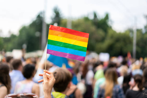 バック グラウンドでぼやけている参加者とのゲイプライド パレードでゲイの虹色の旗 - homosexual rainbow gay pride flag flag ストックフォトと画像