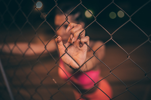 One woman, young and fit woman, training outdoors at night alone, standing by the chainlink fence.