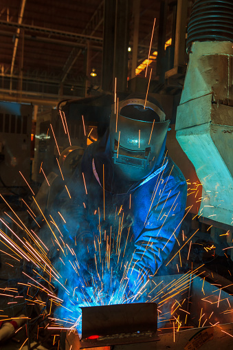 Close up of unrecognizable manual worker cutting iron with a saw in a workshop.