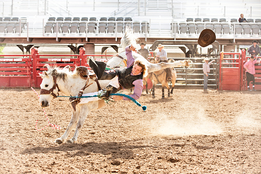 Young cowboy being thrown from a saddle bronc at a summer morning rodeo. Cowboy hat flying through the air.